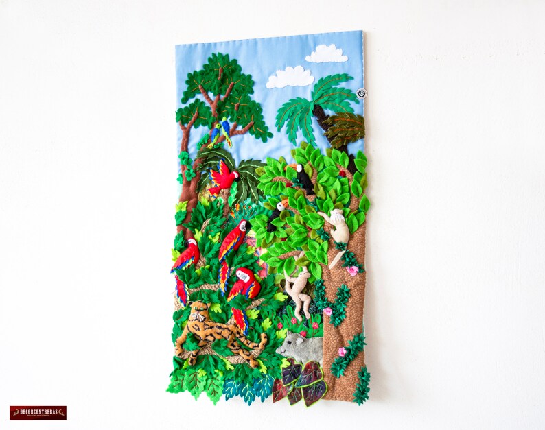 May include: A colorful felt wall hanging depicting a jungle scene with parrots, monkeys, a jaguar, and a toucan. The background is a blue sky with white clouds.