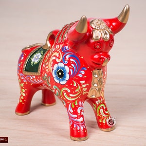 May include: A red ceramic bull figurine with gold accents and intricate floral designs painted in red, white, blue, green, and yellow.