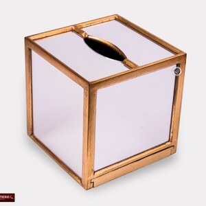 K&ouml;nnte beinhalten: Ein quadratischer Taschentuchbox-Bezug mit goldenem Rahmen und wei&szlig;em Innenraum. Der Bezug hat einen Schlitz f&uuml;r Taschent&uuml;cher und einen kleinen dekorativen Knopf an der Seite.