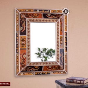 Può includere: Uno specchio decorativo con una cornice colorata dipinta a mano. La cornice presenta intricati motivi floreali e geometrici in tonalità di arancione, marrone e oro. Lo specchio è rettangolare e ha un bordo bisellato.