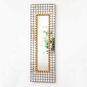 May include: A rectangular mirror with a gold frame and a grid pattern of small squares. The mirror is reflecting a room with a plant in a blue pot.