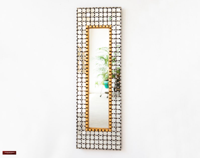May include: A rectangular mirror with a gold frame and a grid pattern of small squares. The mirror is reflecting a room with a plant in a blue pot.