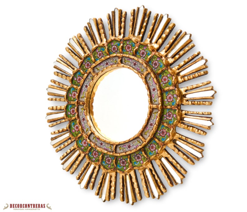 May include: A gold sunburst mirror with a round, mirrored center and a decorative border of green, pink, and white floral designs.