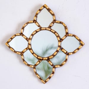 May include: Decorative wall mirror with a gold-colored frame. The mirror has a central circular mirror surrounded by eight smaller mirrors in a floral design. The frame has a textured, ornate appearance, adding a touch of elegance to the piece.