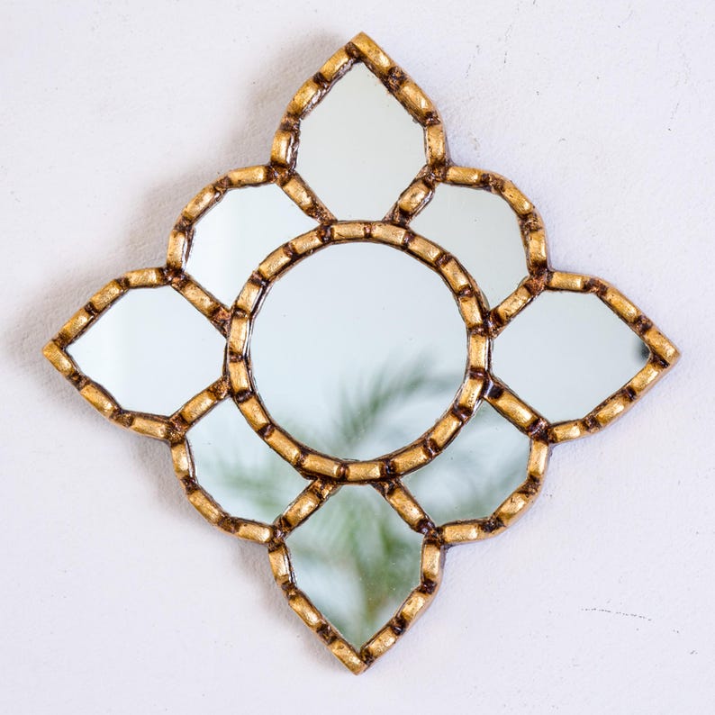 May include: Decorative wall mirror with a gold-colored frame. The mirror has a central circular mirror surrounded by eight smaller mirrors in a floral design. The frame has a textured, ornate appearance, adding a touch of elegance to the piece.