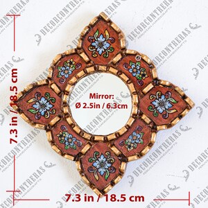 May include: A decorative, handcrafted mirror with a round center and a unique, floral-shaped frame. The mirror is 7.3 inches (18.5 cm) wide and tall, with a 2.5-inch (6.3 cm) diameter mirror. The frame features a brown background with floral designs and gold accents.