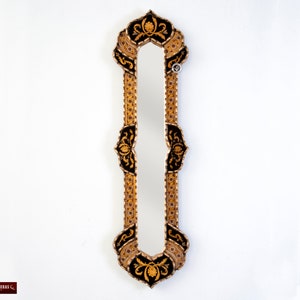 May include: A tall, ornate mirror with a black and gold frame. The frame is decorated with intricate floral designs. The mirror has a rectangular shape with a slightly arched top.