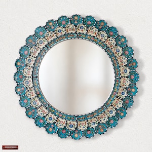 May include: A round wall mirror featuring a decorative frame with a scalloped edge. The frame is adorned with intricate floral patterns in shades of turquoise, cream, red, and blue, arranged in repeating segments around the central glass surface.