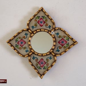 Puede incluir: Un espejo decorativo con un marco blanco y dise&ntilde;os florales en tonos de rosa, azul y verde. El marco tiene forma de estrella de cuatro puntas.
