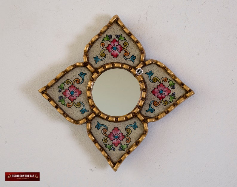 Puede incluir: Un espejo decorativo con un marco blanco y dise&ntilde;os florales en tonos de rosa, azul y verde. El marco tiene forma de estrella de cuatro puntas.