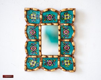 May include: A small, decorative mirror with a teal frame. The frame is intricately carved and painted with gold accents and colorful floral designs.
