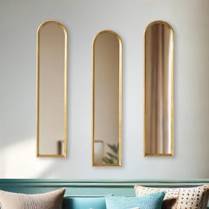 May include: Three tall, arched mirrors with gold frames are mounted on a light gray wall. The mirrors have a rectangular shape with a rounded top. The gold frames add a touch of elegance to the mirrors.