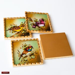 May include: Set of four square coasters with gold frames. Each coaster features a different bird illustration on a green background with small orange berries. The coasters are made of glass and have a gold-colored frame.