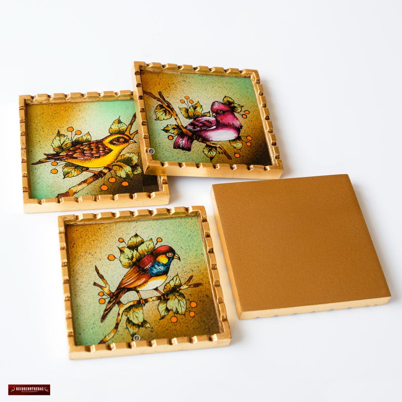 May include: Set of four square coasters with gold frames. Each coaster features a different bird illustration on a green background with small orange berries. The coasters are made of glass and have a gold-colored frame.