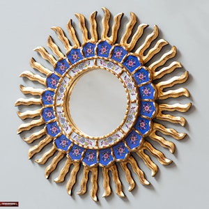 May include: A round mirror with a gold sunburst frame and a blue and white floral design. The mirror is surrounded by a ring of blue and white tiles with floral patterns.