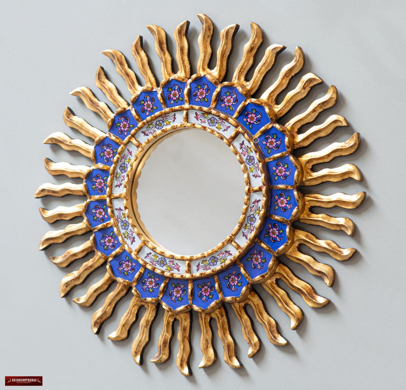 May include: A round mirror with a gold sunburst frame and a blue and white floral design. The mirror is surrounded by a ring of blue and white tiles with floral patterns.