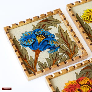 May include: Set of four coasters with a gold trim and a white background. Each coaster features a different floral design with blue, yellow, and orange flowers.