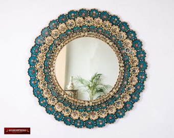 May include: A round mirror with a decorative frame made of teal and cream colored tiles. The tiles are decorated with gold paint and floral designs.