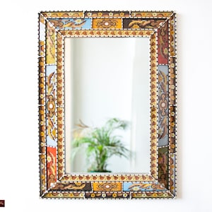 Pode incluir: Um espelho decorativo com uma moldura colorida e estampada. A moldura é feita de azulejos com desenhos florais e geométricos em tons de azul, amarelo, laranja e marrom.