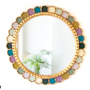 Peut inclure: Un miroir rond doré avec un cadre festonné coloré. Le cadre est composé de morceaux de verre individuels dans des tons de vert, bleu, violet et crème.