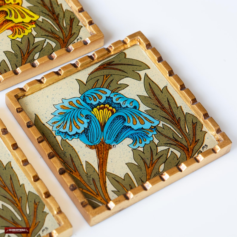 May include: Four square coasters with a gold frame and a floral design. The coasters feature a blue and yellow flower with green leaves on a cream background.