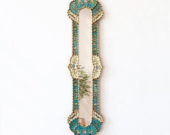May include: A tall, narrow mirror with a decorative frame. The frame is made of wood and is painted in shades of turquoise, white, and gold. The frame is decorated with intricate floral patterns and small birds.
