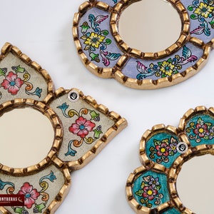 Puede incluir: Tres espejos de pared decorativos con marcos dorados ornamentados y dise&ntilde;os florales coloridos. Los espejos tienen forma de flor, media luna y estrella.