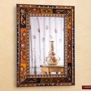 May include: A decorative mirror with a colorful, ornate frame featuring floral and geometric patterns. The frame is made of wood and has a distressed finish. The mirror is rectangular and has a beveled edge.