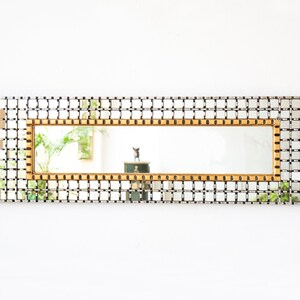 May include: A rectangular mirror with a gold frame and a grid pattern. The mirror is surrounded by a silver grid pattern.