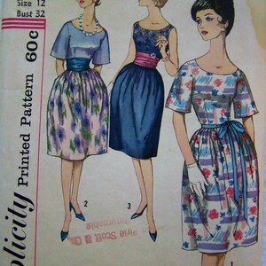 May include: A vintage sewing pattern for a dress with three different styles. The pattern is for size 12 and bust 32. The pattern is printed on a white background with pink and blue accents. The text "Simplicity Printed Pattern 60c" is printed on the left side of the pattern.