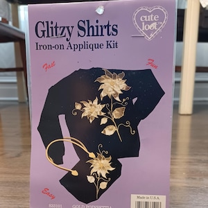 May include: A package for a "Glitzy Shirts" iron-on applique kit featuring a gold poinsettia design. The package includes the text "cute loot" and "Fast, Easy, Fun". The product number is S33101 and the UPC code is 081497 33101 3.