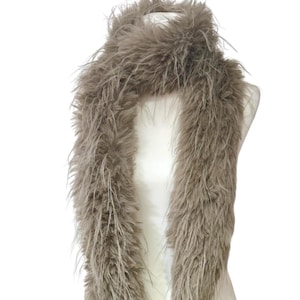 May include: A long, fluffy, taupe-colored boa scarf draped over a mannequin. The scarf is made of soft, feathery material, creating a voluminous and textured appearance. The neutral color makes it a versatile accessory.