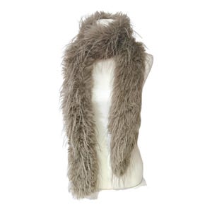 May include: A fluffy, taupe-colored scarf is draped over a white mannequin. The scarf is made of long, soft fibers, creating a textured, voluminous appearance. The scarf is designed to be worn around the neck.