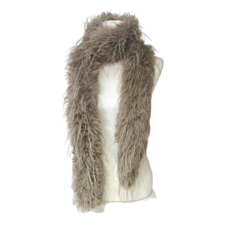 May include: A fluffy, taupe-colored scarf is draped over a white mannequin. The scarf is made of long, soft fibers, creating a textured, voluminous appearance. The scarf is designed to be worn around the neck.