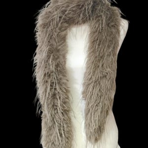 May include: A fluffy, taupe-colored scarf displayed on a white mannequin. The scarf is made of long, soft, feathery material, creating a voluminous and textured appearance. The scarf is draped to showcase its length and drape.