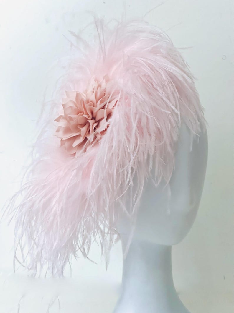 May include: A pink feather headpiece with a blush-colored fabric flower.