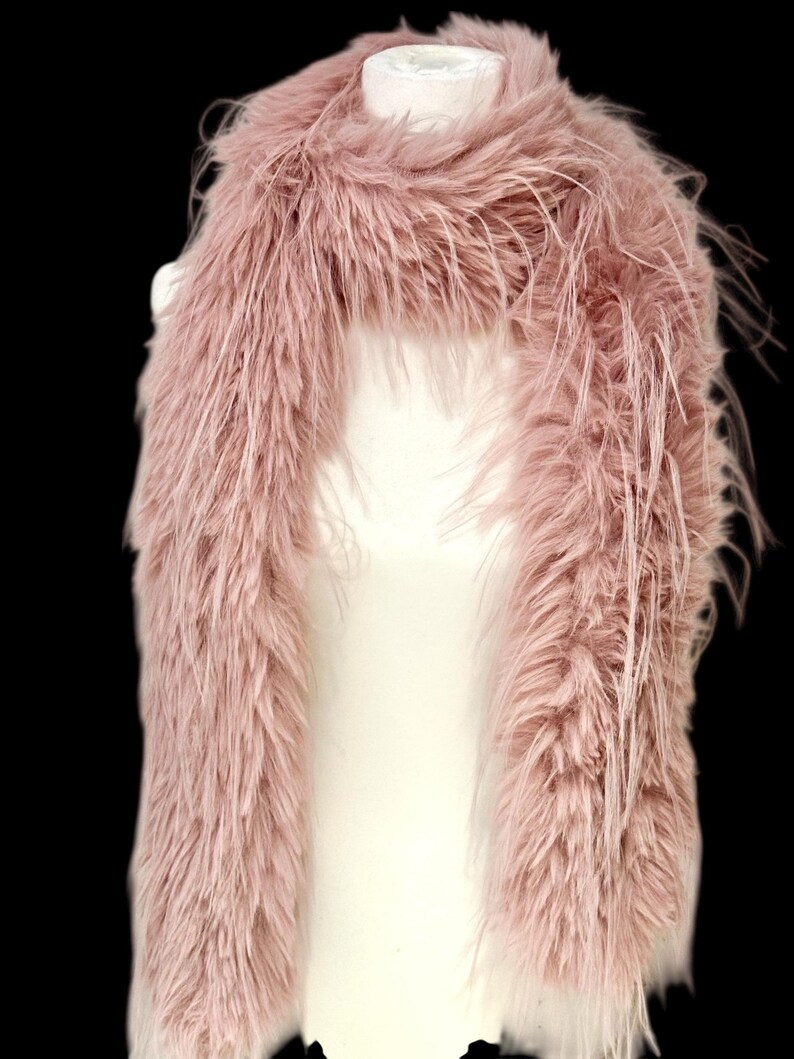 May include: A dusty rose faux fur scarf displayed on a white mannequin. The scarf is long and fluffy, with a soft, textured appearance. The faux fur has a slightly uneven texture, adding to its visual appeal. The background is black.