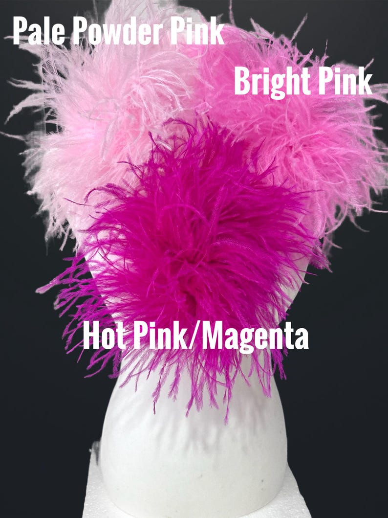 May include: Three fluffy ostrich feather clusters displayed on a white mannequin head. The feathers are labeled Pale Powder Pink, Bright Pink, and Hot Pink/Magenta. The soft, wispy plumes are arranged in distinct shades of pink, creating a textured look.