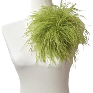 May include: A vibrant lime green feather accessory featuring long, wispy plumes arranged in a dense, rounded cluster. The soft, textured feathers radiate outward from a central point, creating a voluminous and lightweight appearance on a white form.