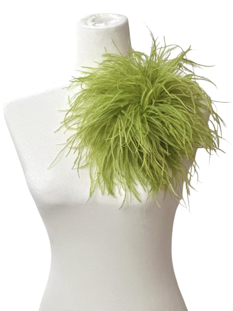 May include: A vibrant lime green feather accessory featuring long, wispy plumes arranged in a dense, rounded cluster. The soft, textured feathers radiate outward from a central point, creating a voluminous and lightweight appearance on a white form.