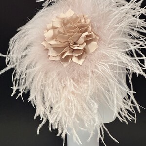 May include: A blush pink feather headpiece with a large beige fabric flower.