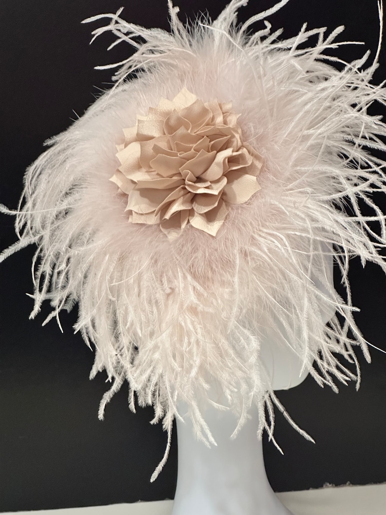 May include: A blush pink feather headpiece with a large beige fabric flower.