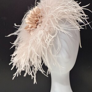 May include: A white feather headband with a beige fabric flower accent. The headband is on a white mannequin head.