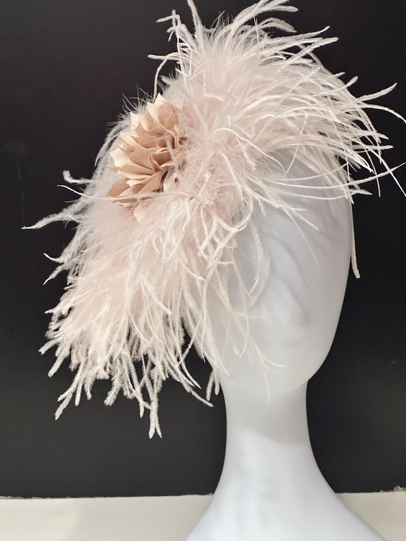 May include: A white feather headband with a beige fabric flower accent. The headband is on a white mannequin head.