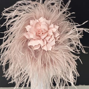 May include: A blush pink feather headpiece with a large, layered, blush pink flower.