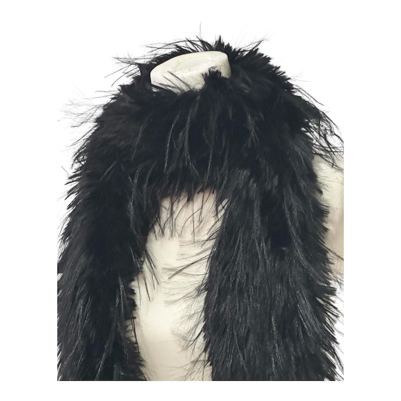 May include: A black feather boa, a long, fluffy accessory. The boa is draped over a white form, showcasing its texture and volume. The feathers are dense and create a dramatic, elegant look.