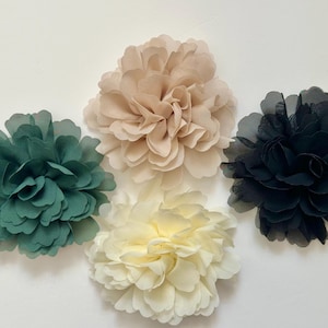 Puede incluir: Cuatro adornos florales de tela en tonos verde, beige, crema y negro. Las flores tienen pétalos en capas, creando una apariencia completa y texturizada. Estas flores decorativas son adecuadas para varios proyectos de manualidades.