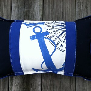 May include: A blue and white pillow with a nautical theme. The pillow features a blue anchor and a compass rose.