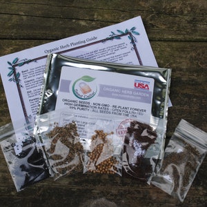 Peut inclure: Un sachet argent&eacute; de graines de jardin d'herbes biologiques avec une &eacute;tiquette qui indique "Jardin d'herbes biologiques, Graines biologiques, Non-OGM, Replanter &agrave; jamais, Taux de germination &eacute;lev&eacute;s, Pollinisation ouverte, Puret&eacute; de 99%, Toutes les graines provenant des &Eacute;tats-Unis". Le sachet est entour&eacute; de cinq petits sachets de graines, chacun contenant un type d'herbe diff&eacute;rent.