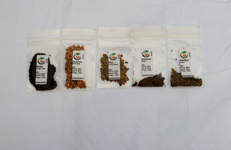 Peut inclure: Cinq petits sachets en plastique transparent contenant diff&eacute;rents types de graines d'herbes. Les sachets sont &eacute;tiquet&eacute;s avec le nom de l'herbe, "Basilic, Grande Feuille", "Coriandre, Croissance Lente", "Aneth, Long Island", "Origan, Italien", et "Persil".